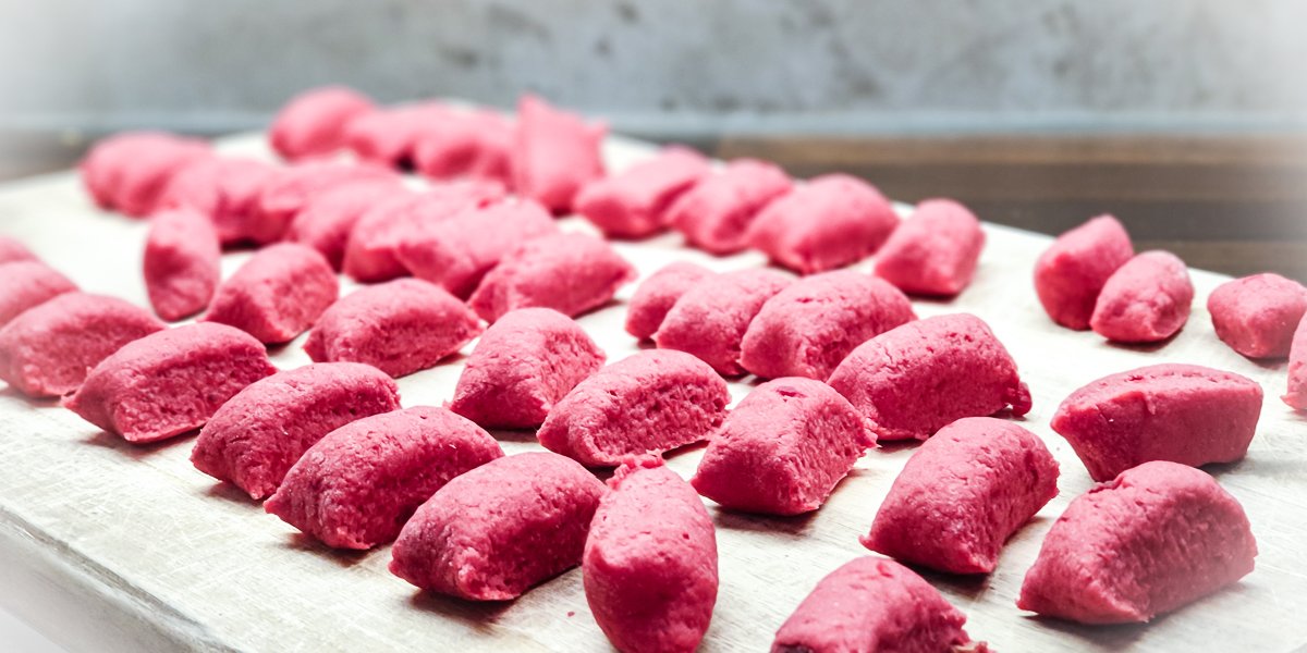frisch geformte rosa rote-rüben-gnocchi auf dem bemehlten holzbrett