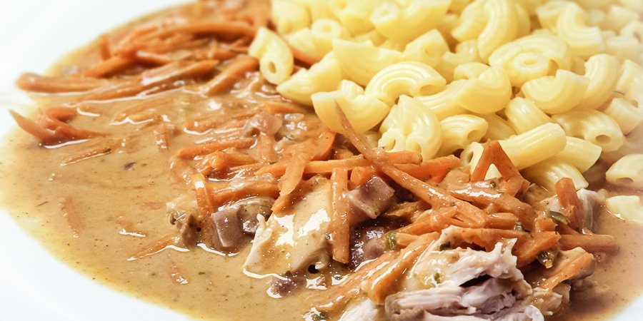 teller mit hörnchennudeln, geraspelten karotten und zartem hühnerfleisch in heller sauce
