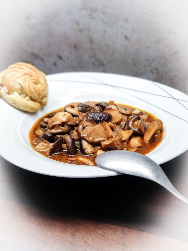 teller schwammerlgulasch mit gebäck und löffel angerichtet