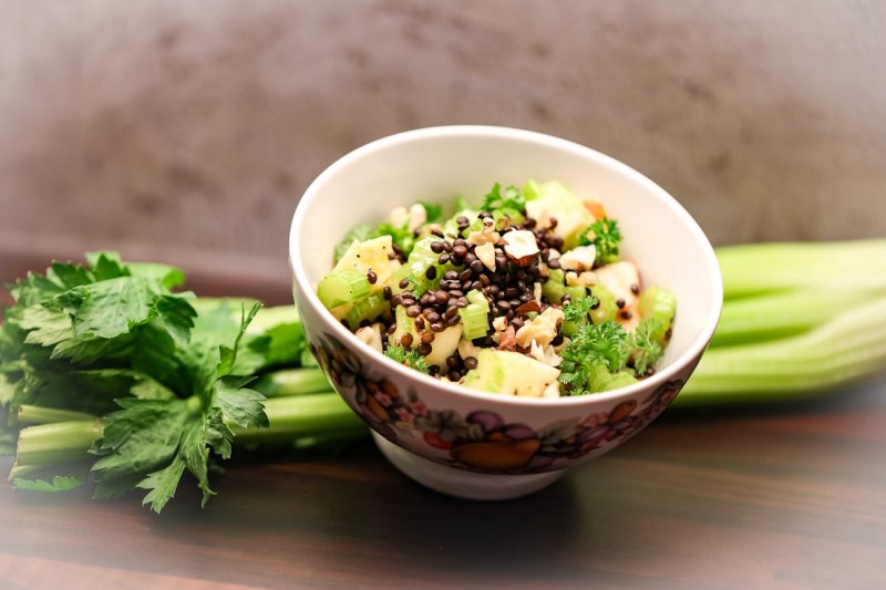© 2020 Sabine Nußbaumer Schüssel mit fertigem Salat aus mit frischen Staudensellerie-Stangen, Äpfeln, Nüssen, Linsen und Honig-Limetten-Dressing