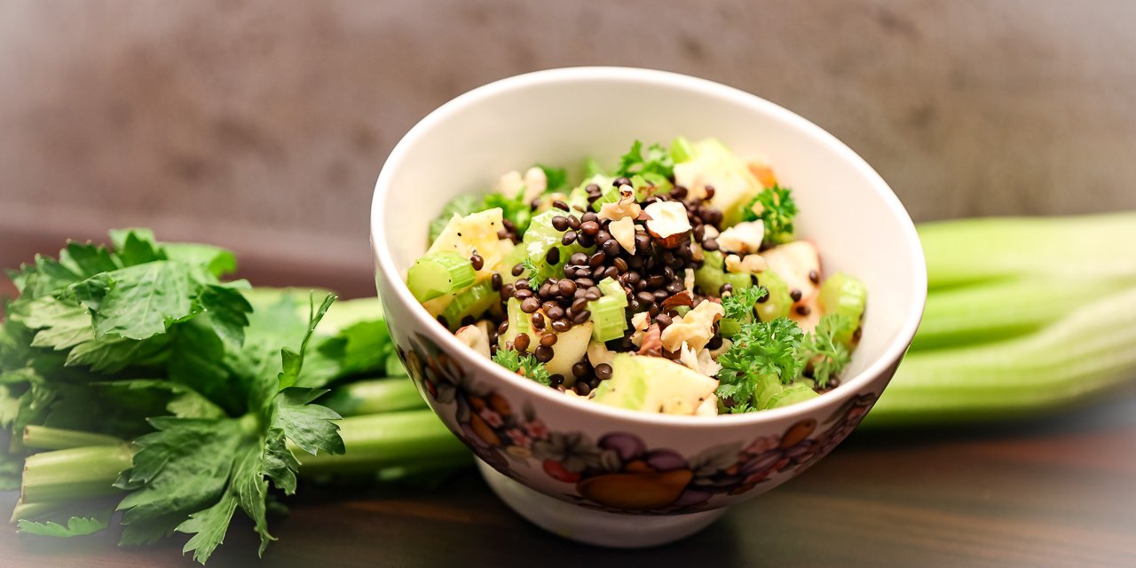 Schüssel mit fertigem Salat aus mit frischen Staudensellerie-Stangen, Äpfeln, Nüssen, Linsen und Honig-Limetten-Dressing