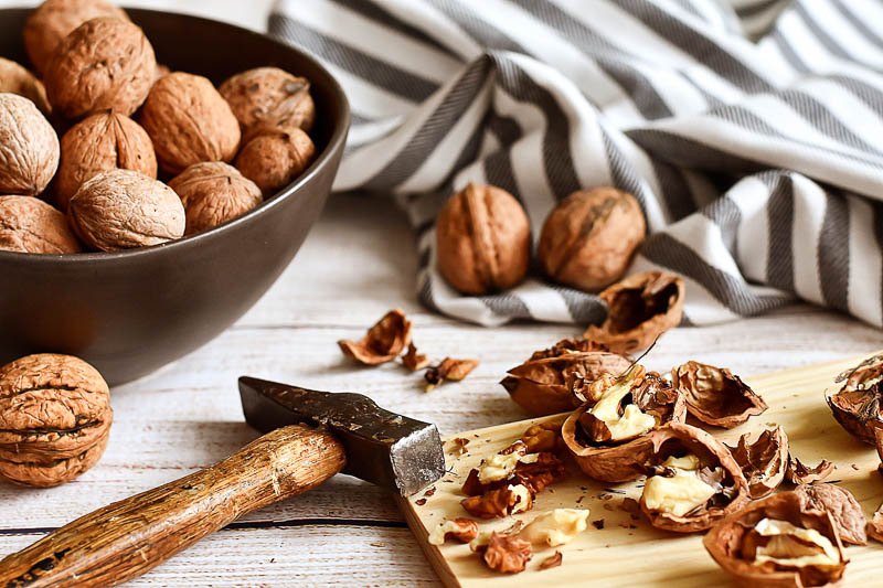 Superfood Walnüsse eine Schüssel voll Walnüsse, davor liegt ein Brett mit bereits geknackten Nüssen und ein kleiner Hammer