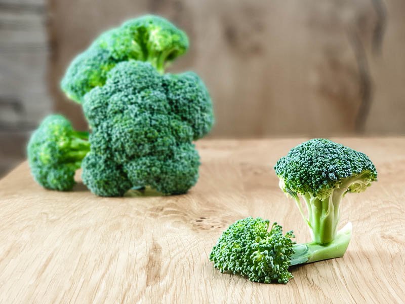Superfood Brokkoli Brokkoli im Hintergrund mit zwei kleinen Röschen im Vordergrund arrangiert