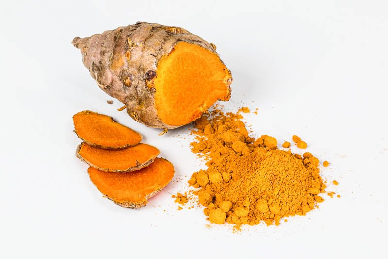 Superfood Kurkuma Aufgeschnittene kräftig orange Kurkumawurzel mit davor etwas Kurkumapulver verstreut